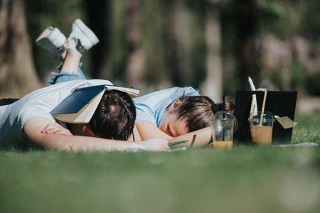 Young couple relaxing together on the grass with school books, taking a break from studyingの写真素材