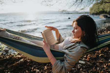 Young girl enjoying a lovely book in a hammock by the lake at sunsetの写真素材