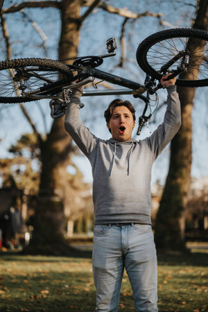 Triumphant young man lifting bicycle overhead in a park settingの写真素材