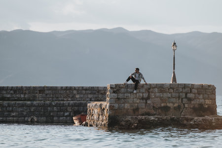 Man enjoying serene moment on stone pier by the lake during a peaceful vacation tripの写真素材
