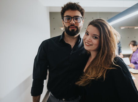 Young professional couple posing in a modern office environment, smiling at the camera