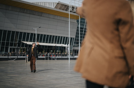 Cheerful businessperson waving for a taxi outside modern buildingの写真素材