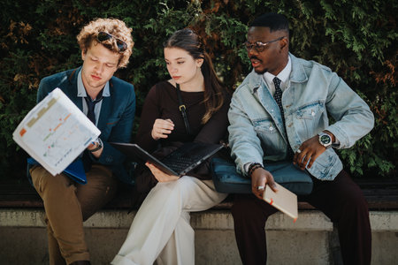 Three business professionals review documents and data outdoor on a sunny dayの写真素材