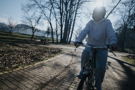 Back lit image of a woman on a bicycle enjoying a leisurely ride through a sun-dappled park, depicting health, fitness, and nature.の写真素材