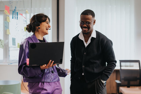 Colleagues sharing a light moment with laptop during an office breakの写真素材