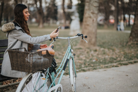 Businesswoman on a break cycling in the park, checking her phoneの写真素材