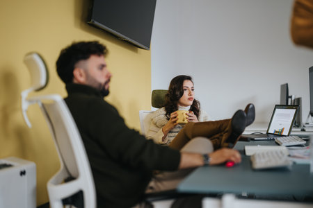 Brunette woman with feet on the desk having a conversation with her male colleague at work.の写真素材