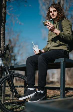 Young man enjoying a sunny day at the park with a smoothie and smart phoneの写真素材