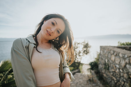 Young joyful woman enjoys a sunny day near the seaside, expressing happiness and relaxationの写真素材