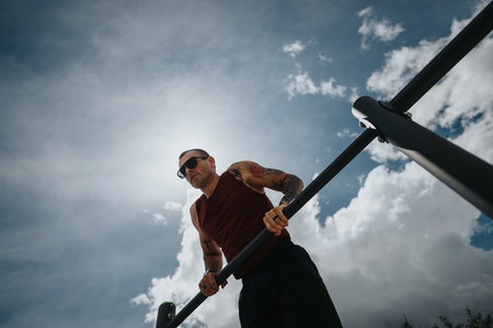 Fit man doing pull-ups at an outdoor park gym on a clear, sunny day