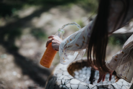 Young girl in floral dress refilling water bottle at well