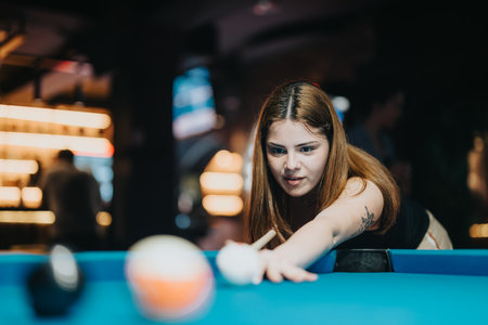 Young woman enjoying a game of pool, focused on strategy and fun with friends in a lively barの写真素材