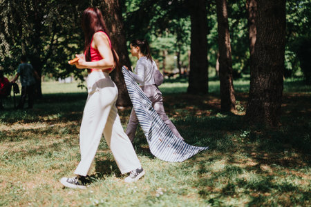 Two women setting up a picnic blanket in a sunny park, enjoying a relaxing day outdoorsの写真素材