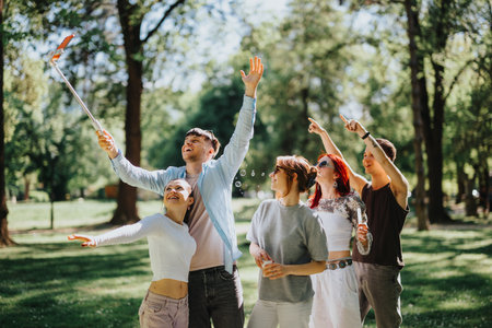 Joyful friends taking a selfie in a sunlit park, celebrating togetherness with bubbles and laughterの写真素材