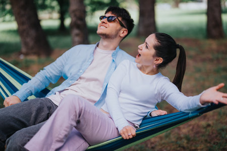 Joyful friends sharing a laugh while relaxing in a hammock at the park on a sunny dayの写真素材