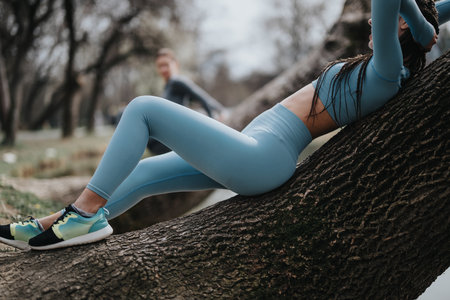 Active sporty woman taking a break on tree trunk during outdoor workoutの写真素材