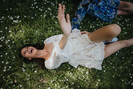 Joyful girl laughing while lying on green grass surrounded by wildflowers in a sunny park