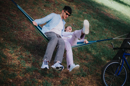 Joyful friends having a great time on a hammock in a sunny parkの写真素材