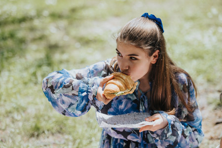 Young girl enjoying a delicious sandwich at a sunny park picnicの写真素材