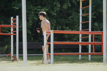 Young man training outdoors at a fitness park with gym equipment on a sunny dayの写真素材