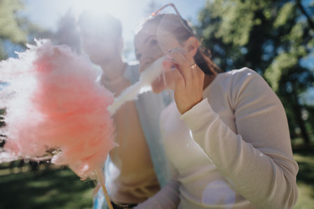 Joyful friends enjoying cotton candy together in a sunny parkの写真素材