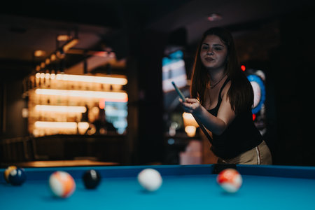 Young woman playing pool in a bar with stylish lightingの写真素材