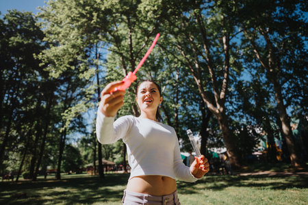 Young woman enjoying a sunny day at the park blowing soap bubbles