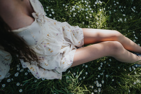 Young girl relaxing in a sunlit park, surrounded by daisies and lush green grassの写真素材