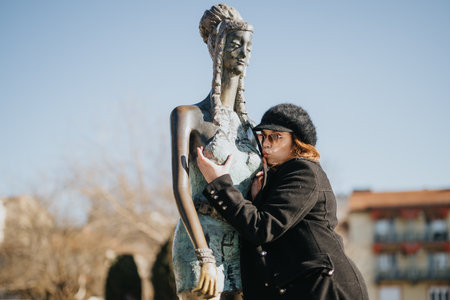 A playful scene of a young woman kissing a statue under a clear, blue sky on a winter day, expressing joy and affection in an urban setting.の写真素材