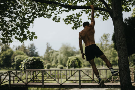 Athletic man hanging from a tree branch in park during outdoor workout