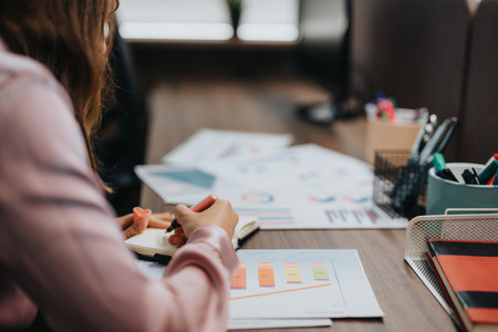 Businesswoman analyzing data with charts and reports on her desk in an office settingの写真素材