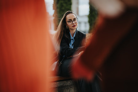 Young woman in glasses sitting on a bench and looking thoughtfully outdoorsの写真素材