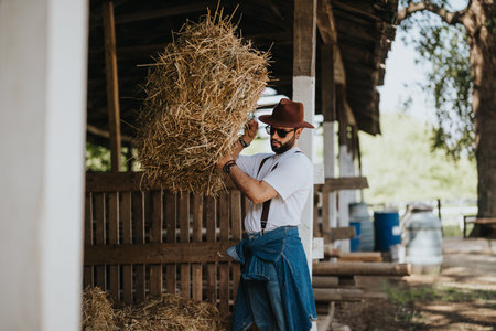 Farmer carrying hay bale on a sunny day on rural farmの写真素材
