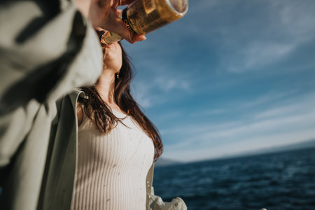 Young woman enjoying a cold drink by the sea on a sunny dayの写真素材