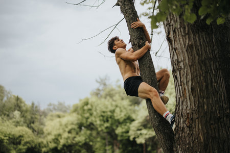 Shirtless man climbing tree in nature, demonstrating outdoor fitness and adventureの写真素材