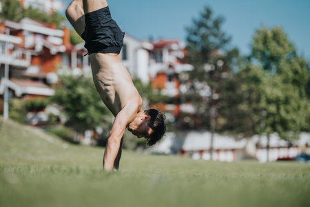 Young man performing a handstand in a grassy park on a sunny day capturing balance and fitnessの写真素材