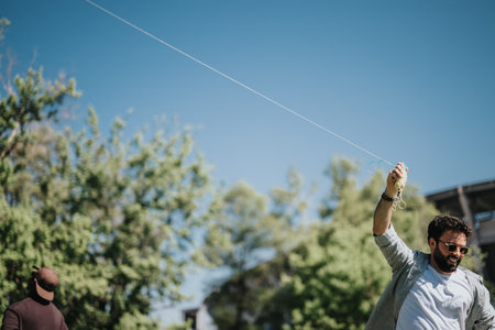Joyful man flying a kite in the park with friends on a sunny dayの写真素材