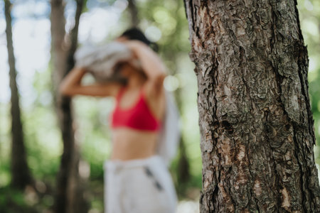 Woman refreshing in forest wearing sports bra, tree bark in focusの写真素材