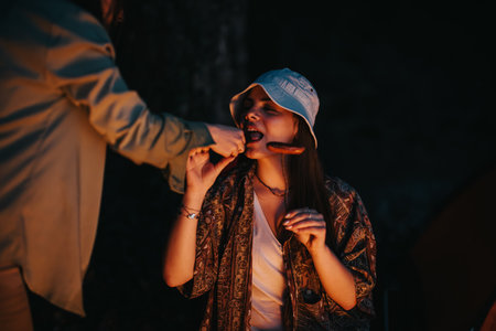 Friends enjoying a joyful dinner by a campfire near a lake at night