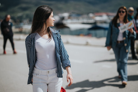 Young woman exploring a seaside town on a sunny day, tourists in the backgroundの写真素材