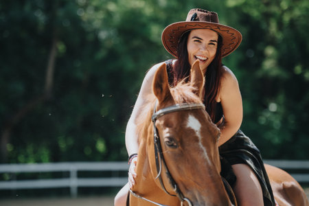 Young woman enjoying horseback riding on a sunny day, wearing a cowboy hat and smiling outdoorsの写真素材