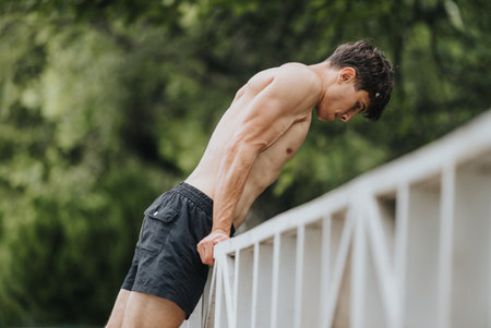 Fit young man doing arm exercises on a bridge in the park