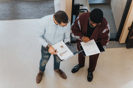 Overhead view of a multiracial business teammates discussing graphs and charts with a younger colleague holding a digital tablet.の写真素材