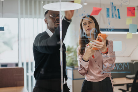 Business colleagues brainstorming with sticky notes on glass in modern office