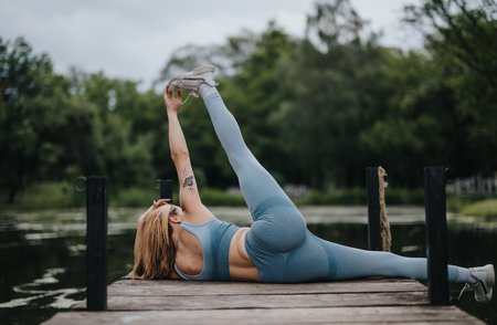 Woman exercising outdoors on wooden pier by the lake in natureの写真素材