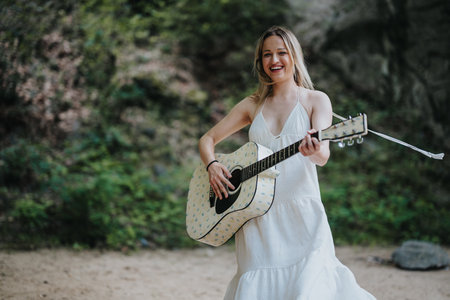 Young woman in white dress enjoying outdoor picnic with guitar in handの写真素材