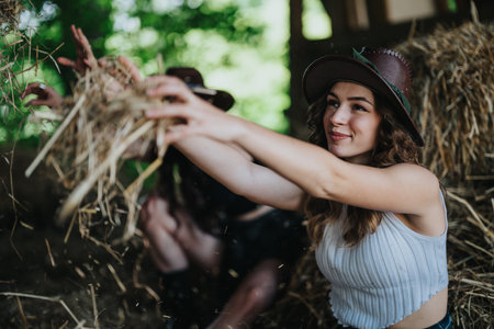 Joyful young woman having fun playing with hay on a sunny day in barnの写真素材