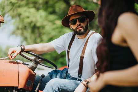 Bearded man in sunglasses and hat driving vintage tractor in rural settingの写真素材