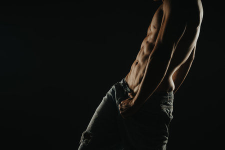 Athletic man showing muscular torso and abs in dramatic lightingの写真素材