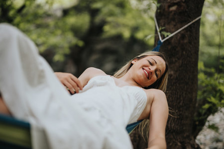 Relaxed young woman smiling while lying in hammock outdoors on a summer dayの写真素材